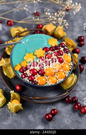 Ciotola di frullato di frutta con polvere di spirulina verde naturale sana decorata con mirtilli rossi, phisalis e frutti kaki e quinoa purè Foto Stock