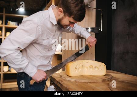 Giovane lavoratore fetta di formaggio maasdam su tavola di legno in negozio di formaggio Foto Stock