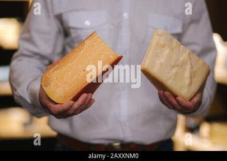 Un bell'uomo con bearded tiene in mano diversi tipi di formaggio invecchiato nel negozio di formaggi Foto Stock