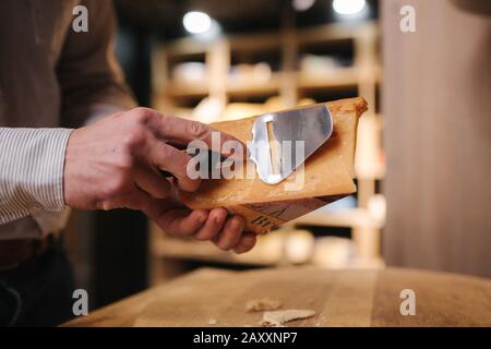 Uomo affettare un pezzetto di formaggio per il gusto. Giovane lavoratore utilizzare coltello speciale per il formaggio Foto Stock