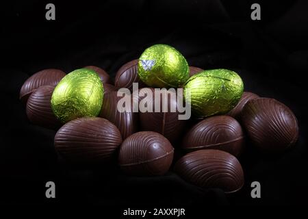 Pila di calce di colore verde o giallo stagnola avvolto e confezionato le uova di Pasqua di cioccolata contro uno sfondo nero. Foto Stock