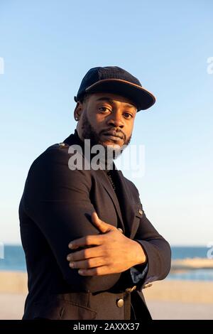 Vista frontale di un giovane africano americano barbuto con le braccia incrociate guardando la macchina fotografica in giornata di sole Foto Stock