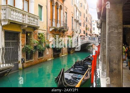 I turisti attraversano un ponte su un piccolo canale con una gondola parcheggiata nel centro storico di Venezia. Foto Stock