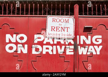 Cartello con camera in affitto per appendere fuori di una vecchia porta di metallo dipinta di rosso. Non c'è parcheggio in auto scritto sul cancello, visto nelle Filippine, in Asia Foto Stock