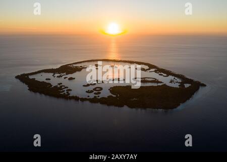 Visto al tramonto, una remota isola tropicale, Kofiau, nel mare di Molucca è circondata da un sottile margine di foresta di mangrovie che circonda una laguna poco profonda. Foto Stock