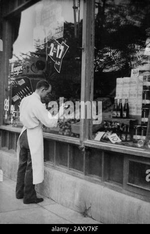 Un droghiere in un deposito di Chicago Kroger dipinge un'esposizione di prezzi sulla sua finestra del deposito, ca. 1940. Foto Stock