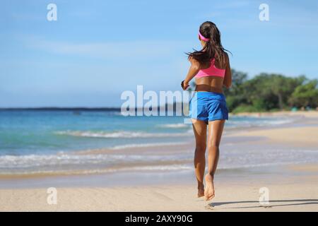 Donna runner che corre a piedi nudi sulla sabbia in spiaggia. Atleta femminile con gambe sottili che si allontanano, vista dalla parte posteriore, sulla destinazione tropicale di viaggio. Foto Stock