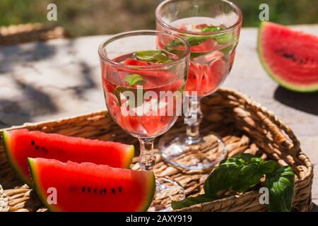 Su un tavolo in giardino in un cesto ci sono due bicchieri di limonata e affettato di cocomero Foto Stock