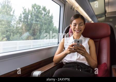Sorridere donne d'affari asiatiche utilizzando l'app per smartphone social media mentre si è in viaggio per lavorare in treno. Donna seduto nel trasporto godendo di viaggio. Foto Stock