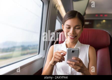 Buon businesswoman asiatico che utilizza l'app per telefono cellulare per inviare SMS o giocare ai videogiochi mentre si è in viaggio per lavorare in treno. Donna seduto nel trasporto godendo di viaggio. Foto Stock