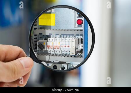 Tecnico Maschile Che Esamina La Scatola Fusibili Con Lente Di Ingrandimento Foto Stock