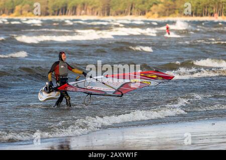 Tallinn, Estonia - 18 ottobre 2008: Un windsurf in una tuta porta una tavola a vela fuori dal mare. Onde in mare. Lo sfondo è sfocato. Foto Stock