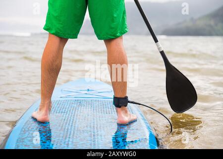 Paddleboard uomo paddling su SUP stand up paddle board sul lago. Primo piano di piedi e gambe. Foto Stock