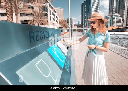 Una ragazza smista e getta rifiuti in una stazione stradale per riciclare rifiuti di plastica. Concetto di conservazione dell'ambiente Foto Stock