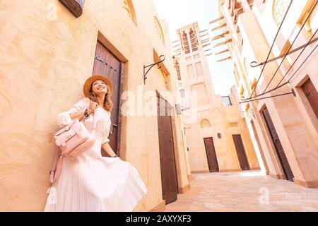 Ragazza asiatica felice in abito bianco a piedi tra le strette strade della città vecchia da qualche parte in Medio Oriente. Destinazioni di viaggio e concetto di turismo Foto Stock