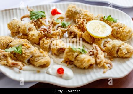 Calamari fritti e martoriati con salsa di catrame e limone serviti su un piatto bianco di ceramica. Foto Stock