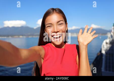 Donna asiatica che parla con l'app di telefonia mobile per chat video o scatta foto selfie per i social media. Giovane donna d'affari che usa lo smartphone sorridente felice in spazi aperti soleggiati. Donna professionale urbana. Foto Stock