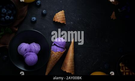 Colpo di testa di dessert estivo con gelato al mirtillo, farcitura, cono di waffle e spazio di copia su sfondo nero scrivania Foto Stock