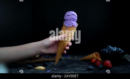 Vista ravvicinata di una ragazza che tiene il cono gelato mirtillo con mirtillo e condimenti su sfondo nero tabella Foto Stock