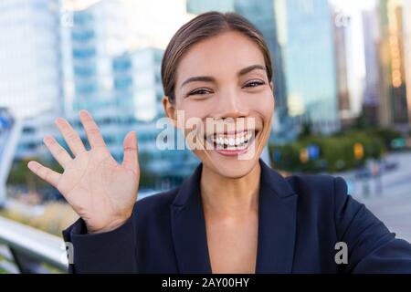 Donna d'affari che scatta foto selfie utilizzando l'app per smartphone per i social media. Giovane donna d'affari che usa uno smartphone sorridente indossa una giacca da vestito all'aperto. Donna professionale urbana. Foto Stock