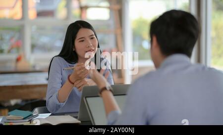 Scatto corto di due imprenditori che consultano sul loro lavoro con i rifornimenti dell'ufficio e del laptop mentre siing opposto l'un l'altro Foto Stock