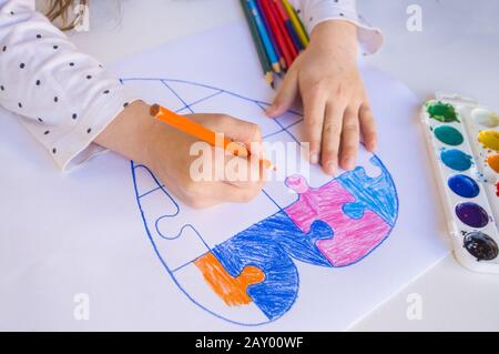 Un bambino sta disegnando cuore colorato con puzzle jigsaw su sfondo bianco come un simbolo di autismo, con matite colorate e acquerelli. Foto Stock