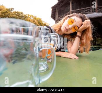 Giovane ragazza asiatica ubriaca con hangover dormire in Biergarten con tazze di birra vuote Foto Stock