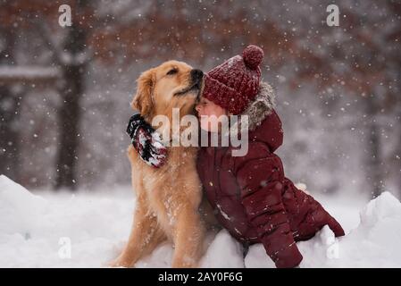 Ragazza seduta nella neve coccolando il suo cane Golden Retriever, Wisconsin, Stati Uniti Foto Stock