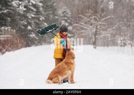 Ragazzo con una pala in piedi con il suo cane nella neve su una lunga strada coperta di neve, Wisconsin, Stati Uniti Foto Stock