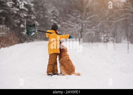 Ragazzo con una pala in piedi con il suo cane nella neve su una lunga strada coperta di neve, Wisconsin, Stati Uniti Foto Stock