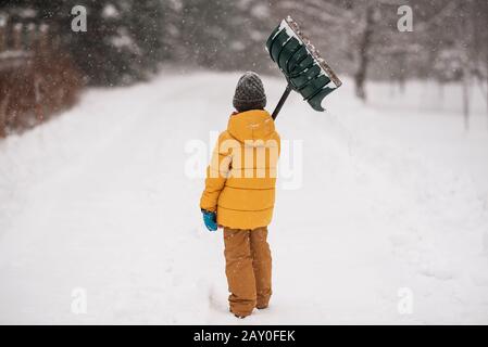 Ragazzo con una pala in piedi nella neve su una lunga strada coperta di neve, Wisconsin, Stati Uniti Foto Stock