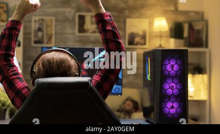 Vista posteriore della donna che vince ai videogiochi mentre gioca a tarda notte. Dispone di un potente PC con ventilatori al neon sul davanti Foto Stock