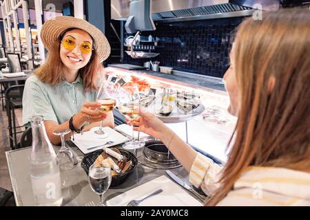 Due amici femminili in un ristorante che mangia ostriche e crostacei e beve vino bianco Foto Stock