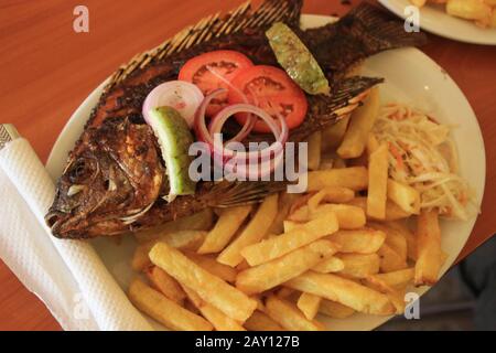 Un piatto tradizionale e gustoso in Uganda sulle rive del Lago Victoria - pesce Tilapia appena fritto e patatine fritte. Foto Stock