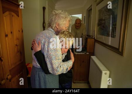 Nonna (83 anni) salutò suo nipote (9 anni) guardato calorosamente dal nonno (86 anni) nel corridoio di casa, Inghilterra, Regno Unito Foto Stock