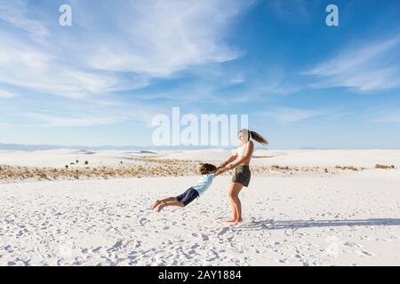 Ragazza teen che oscilla il suo fratello di 6 anni nella sabbia, White Sands Nat'l Monument, NM Foto Stock