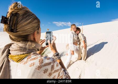 Una donna che fa foto dei suoi bambini con uno smartphone in sabbia bianca paesaggio dune sotto il cielo blu. Foto Stock