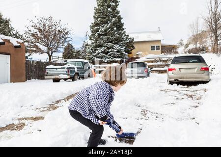 Un ragazzo di sei anni che spalava la neve nel vialetto Foto Stock