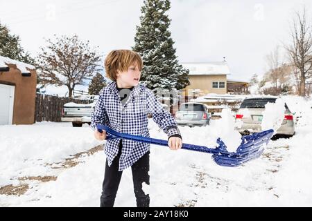 Un ragazzo di sei anni che spalava la neve nel vialetto Foto Stock