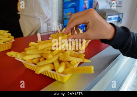 Oosterscheldekering, Paesi Bassi, Agosto 2019. La portata principale in un chiosco di cibo di strada: Patatine fritte. Una porzione è pronta per essere gustata, una mano è t Foto Stock