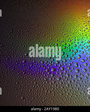 Gocce d'acqua su vetro con sfondo arcobaleno colorato. Rugiada del mattino sulla finestra con un riflesso rifrattivo di luce solare multicolore. Foto Stock