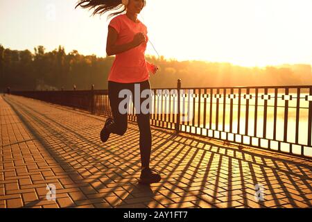 Runner corre sulla strada del sole al tramonto in un parco d'autunno. Foto Stock