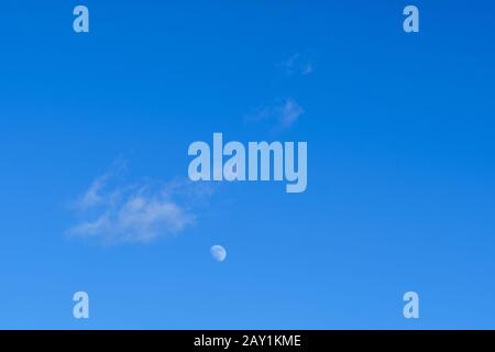 Cielo blu chiaro con una nuvola bianca e la luna come sfondo con spazio di copia. Visto in Baviera, Germania, in una giornata di febbraio soleggiata Foto Stock