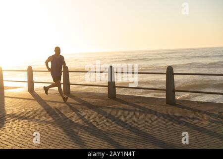 Jogger che corre sul mare al tramonto Foto Stock