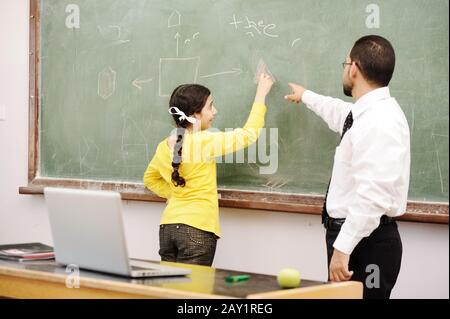 Insegnante che aiuta la scolaretta di fronte a bordo Foto Stock