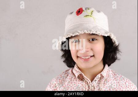 Ragazza sorridente che mostra denti indossando un cappello con fiore rosso Foto Stock