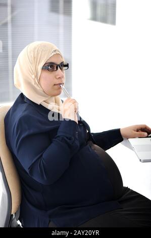 Donna d'affari araba musulmana incinta che lavora in ufficio Foto Stock