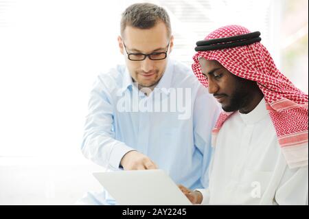Uomini arabi neri e caucasici che lavorano insieme sul laptop Foto Stock