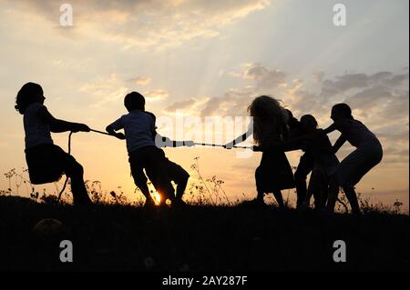 Silhouette, gruppo di bambini felici che giocano su prato, tramonto, estate Foto Stock