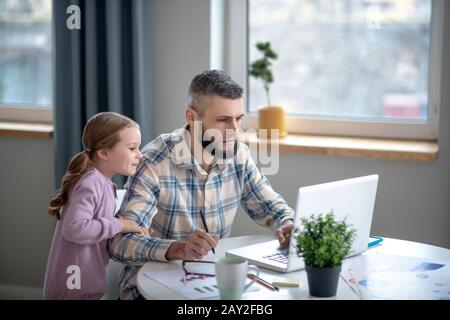 Giovane uomo che lavora dietro un netbook, bambina vicina. Foto Stock